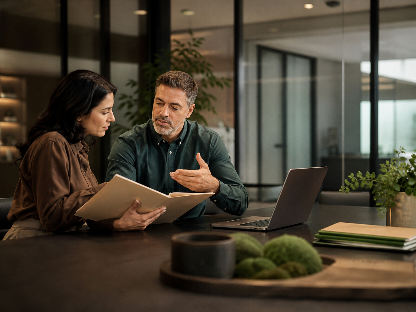Two professionals reviewing a folder and laptop in a meeting room