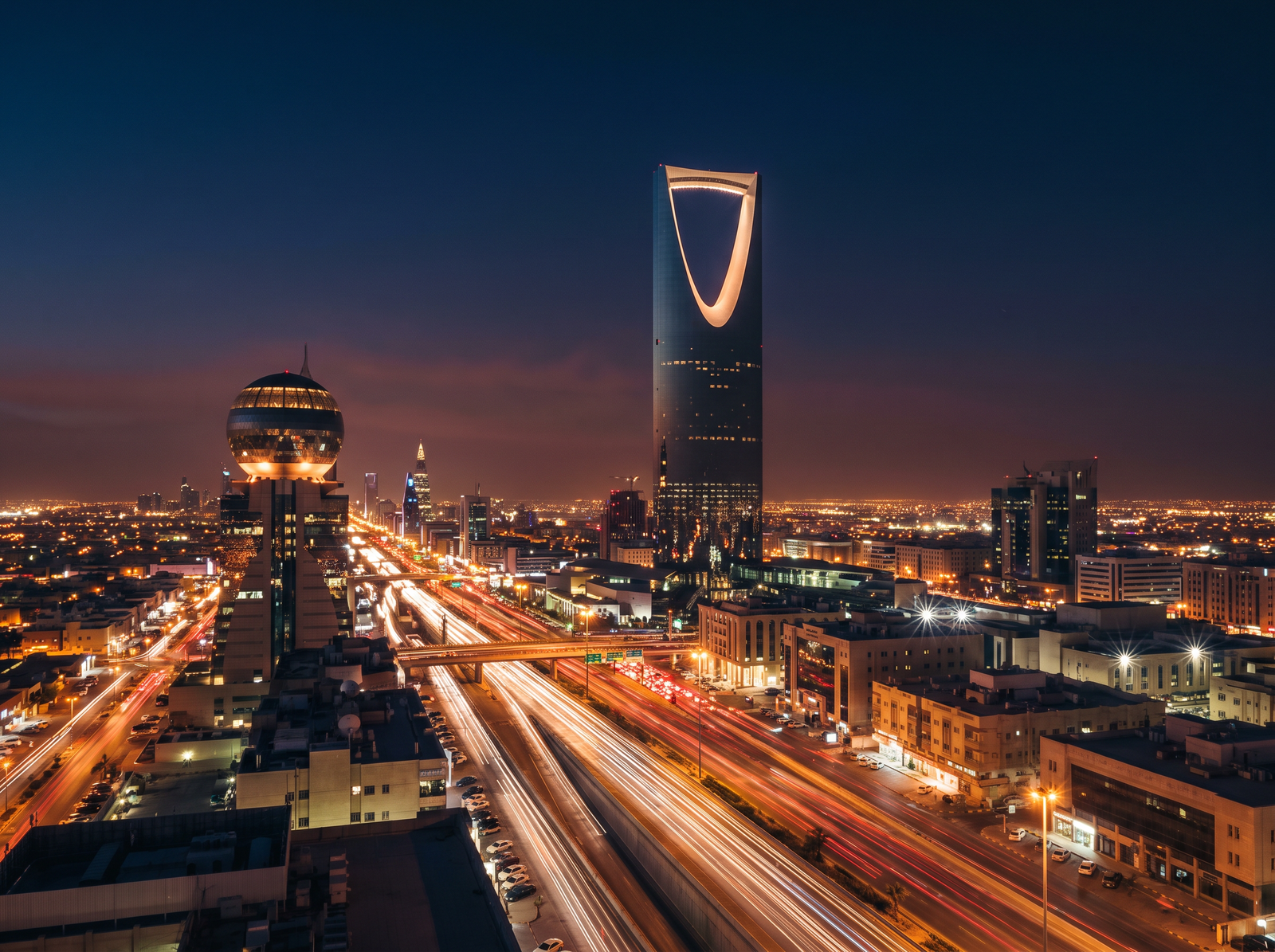 Riyadh skyline at night with the Kingdom Centre tower lit up and light trails on King Fahd Road